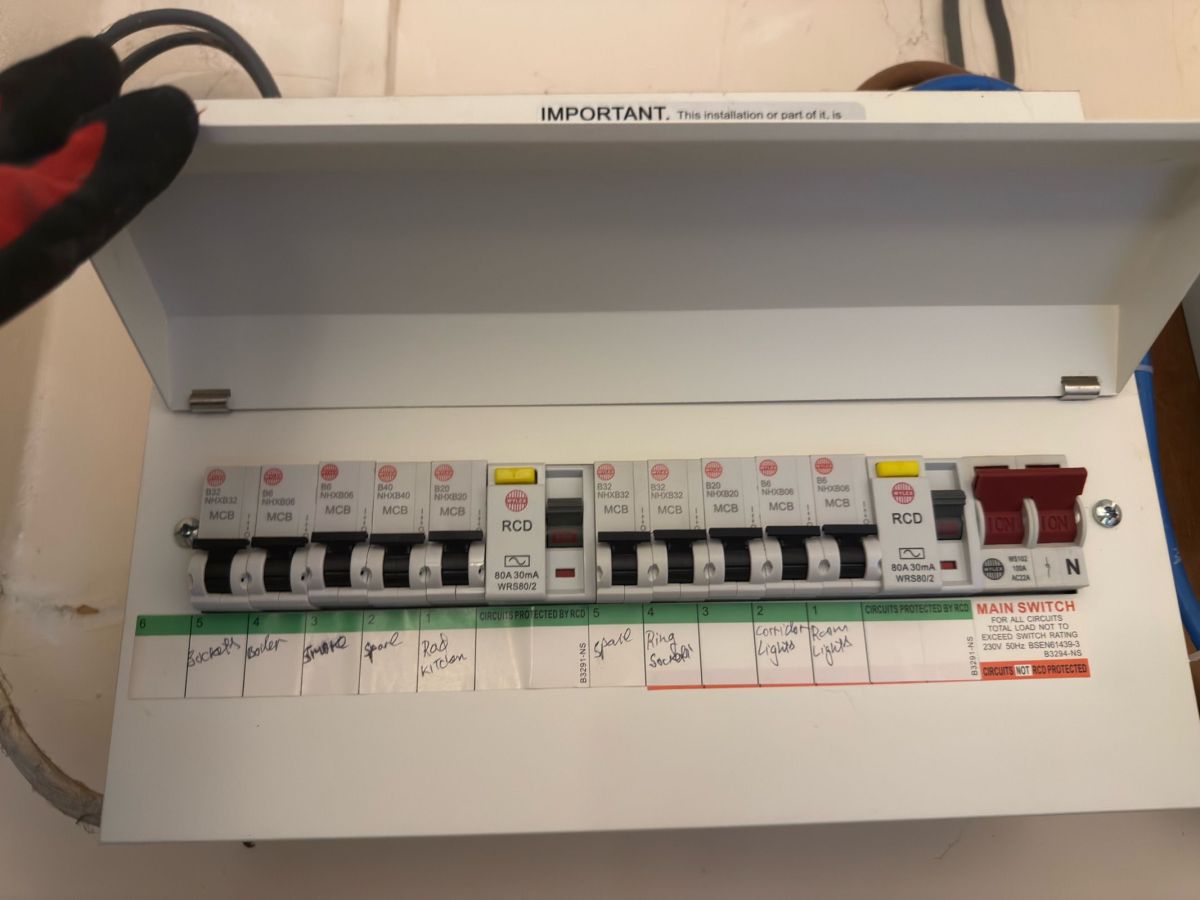 Consumer unit with its lid open showing the periodic inspection notice and labelled circuits